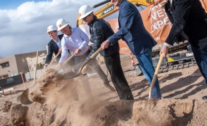 People in construction hats using shovels at a groundbreaking ceremony for a new housing development.