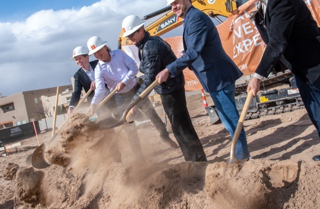 People in construction hats using shovels at a groundbreaking ceremony for a new housing development.